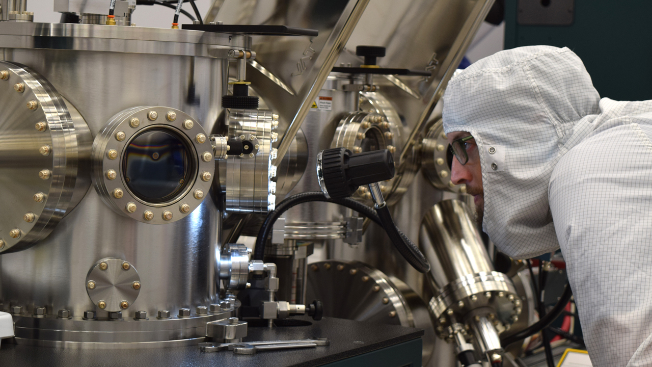 researcher in cleanroom gear investigating a complex nanoscience instrument