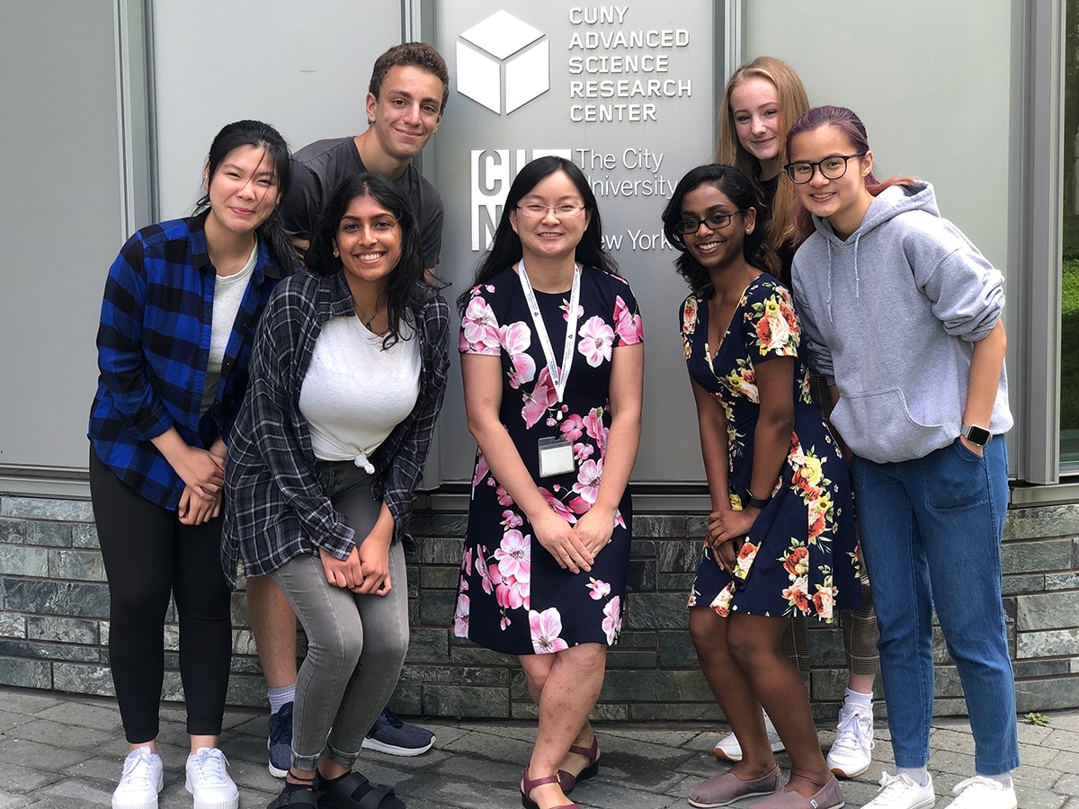 a group of students with Dr. Ye He standing together in front of the CUNY and ASRC logos on the exterior of the ASRC building