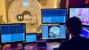 A person staring a screens in a lab that has an MRI machine in the background