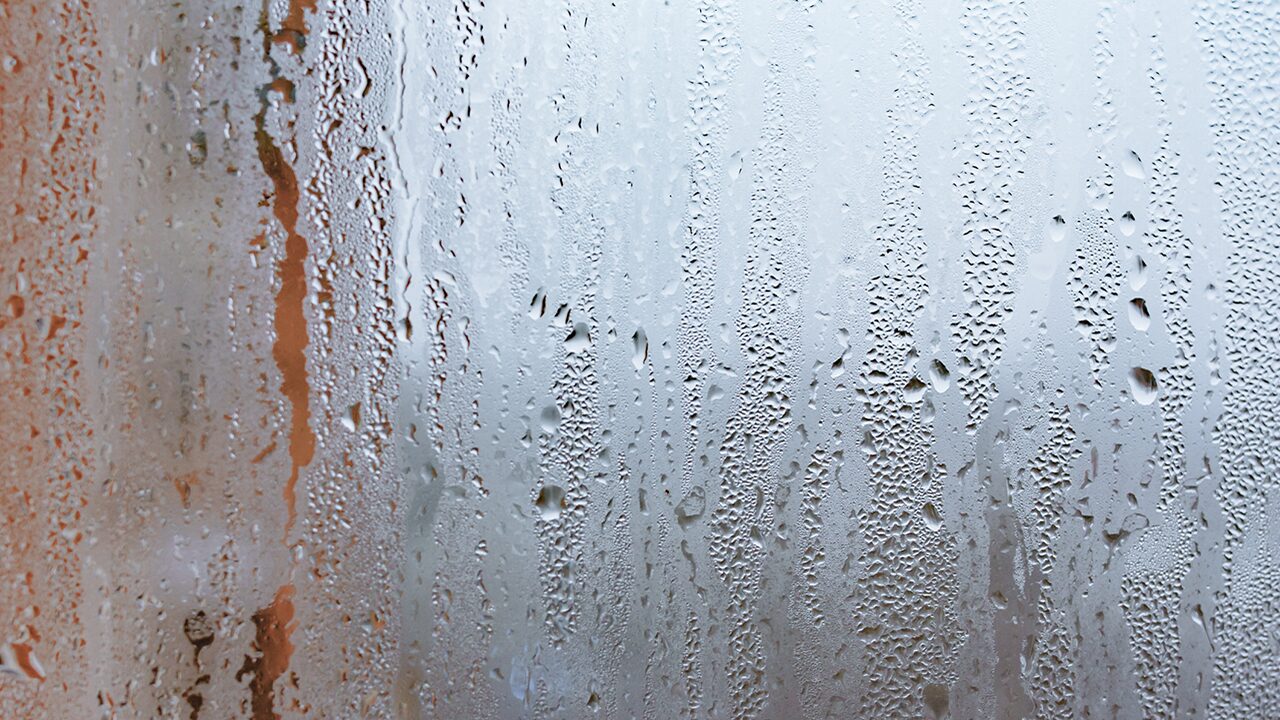 Condensation on a frosted glass surface, featuring numerous droplets and a blurred background.