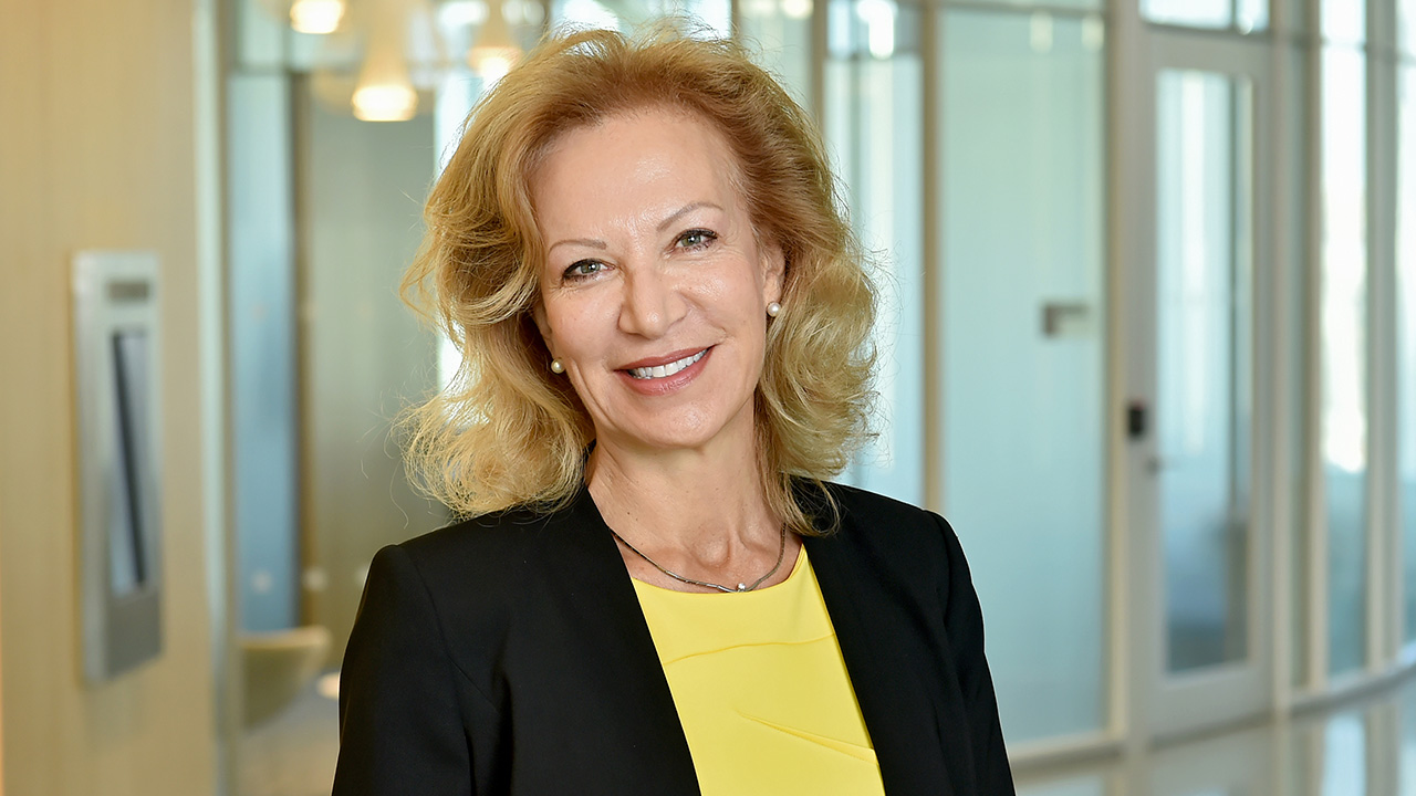 Professor Patrizia Casaccia smiling wearing a black blazer over a yellow blouse, standing in the CUNY ASRC.