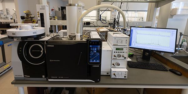 A laboratory setup featuring an analytical instrument, a touchscreen monitor, and various connected devices on a table.