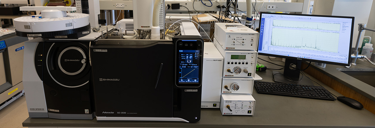 A laboratory setup featuring a Shimadzu GC-2030 gas chromatograph and a monitor displaying spectrometry data.
