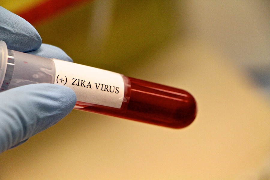 A gloved hand holding a vial labeled Zika Virus