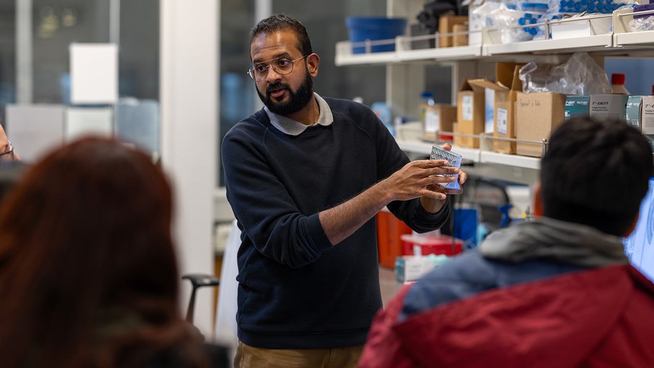 Professor standing in lab holding up equipment talking to students