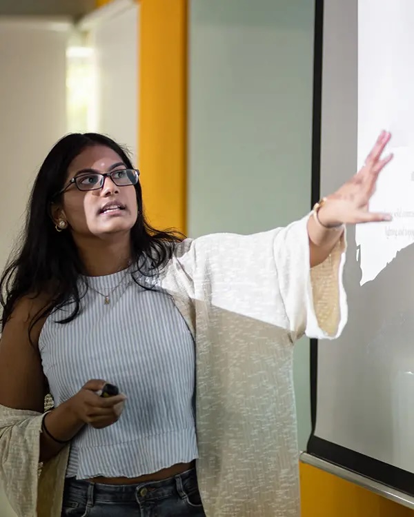 A student giving a presentation in front of a projector screen.