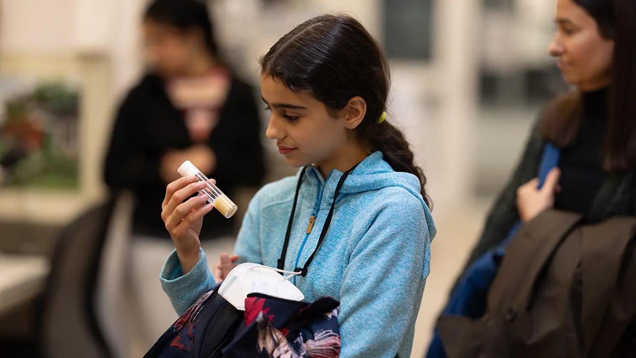A young child holding and looking at tube of gnats in a research lab