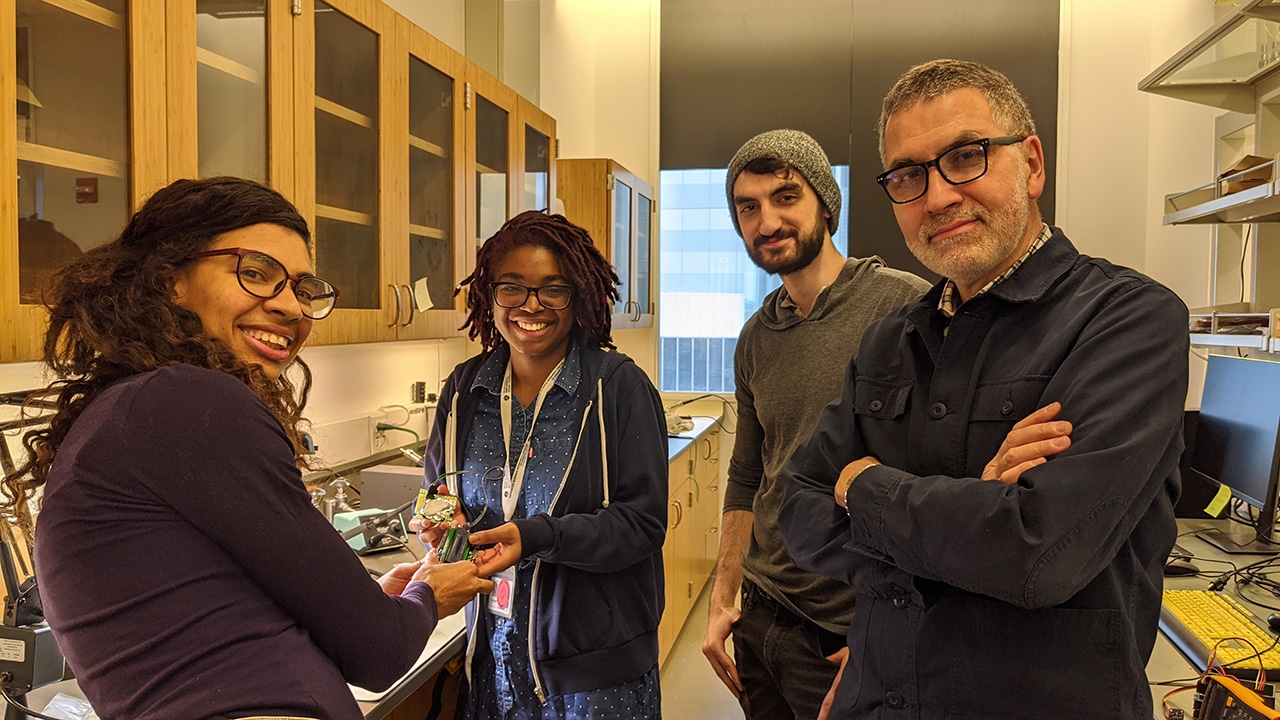 four researchers stand in a lab space, smiling and looking at the camera