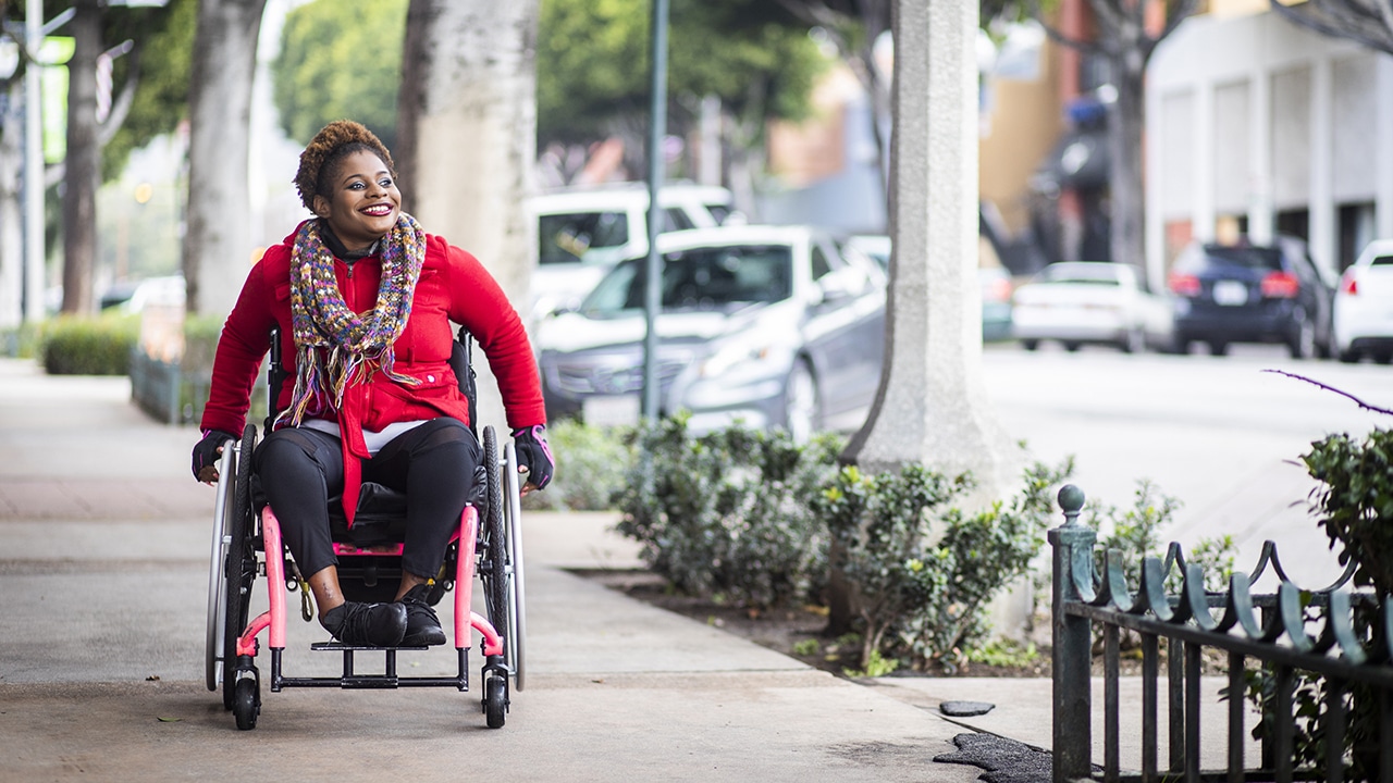 smiling Black woman in a wheelchair, on a sidewalk in a landscaped downtown area