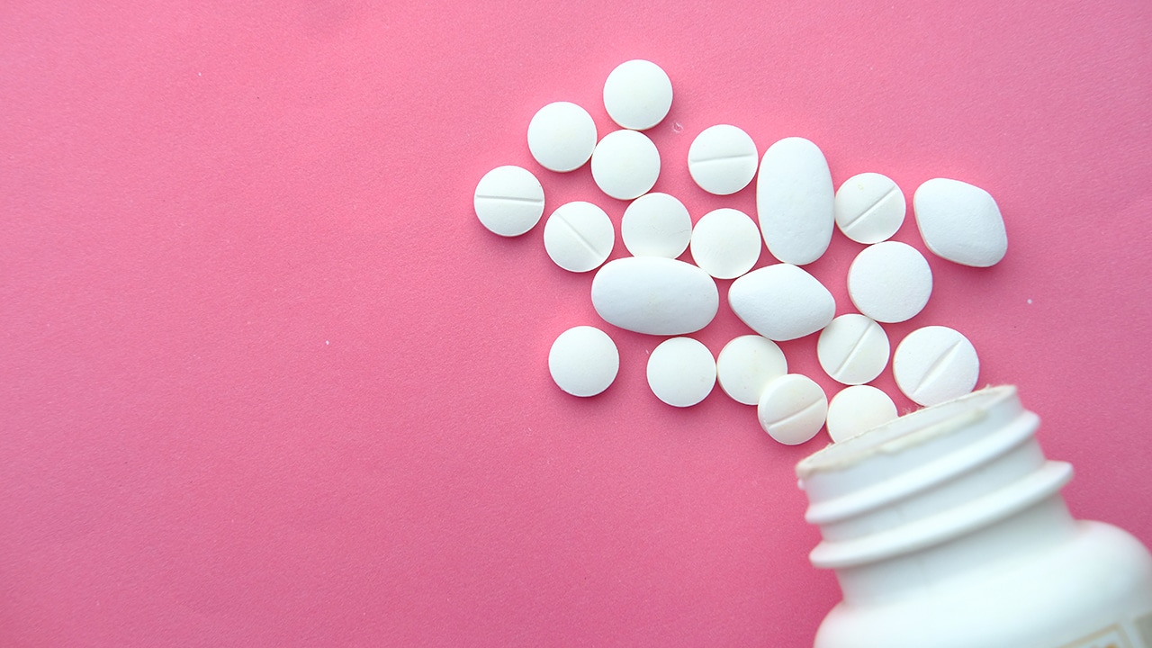 white pill bottle spilling variously shaped white pills onto a flat pink background