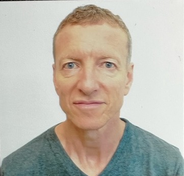 Man with short hair and light skin, wearing a gray V-neck shirt, against a plain white background.